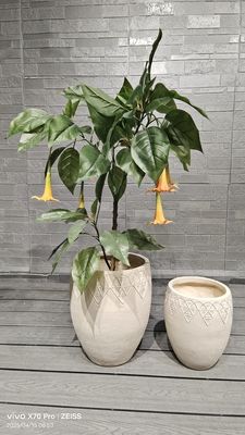 Jardinera cilíndrica de fibra de arcilla beige neutro con intrincada decoración floral